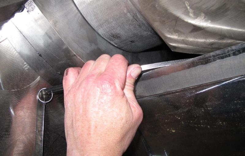 A hand measures a metal surface, the mixer wear, with a feeler gauge, surrod by shiny metallic components
