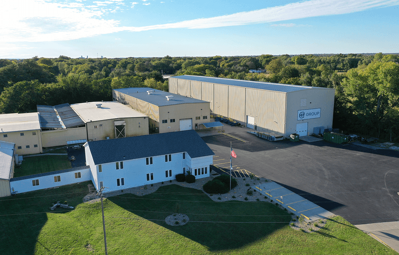 Aerial view of an HF GROUP facility with production halls, office building, and a large paved yard surrounded by greenery.