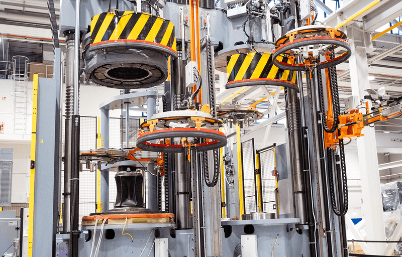 Tyre curing press with multiple press stations, lifting systems, and safety markings.