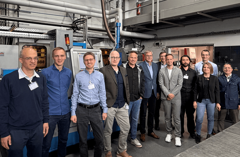 Group of people standing in a technical setting next to machinery and pipes.