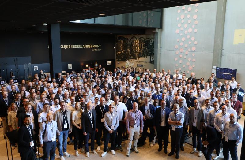A large group of people, dressed in business attire, stands smiling in a spacious, modern atrium with decorative wall art.