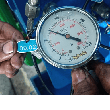 Close-up of a hydraulic pressure gauge: dirty hands check the reading, scale up to 6000 psi, indicating on-site maintenance and troubleshooting.