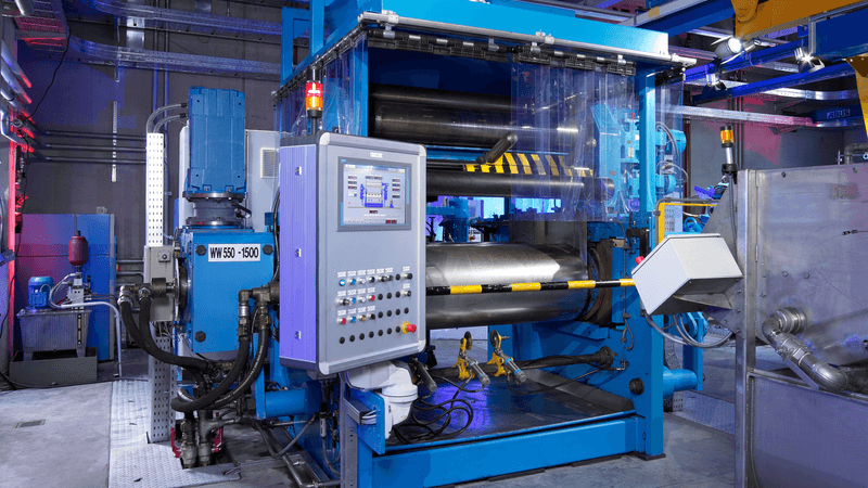 Blue industrial machine with rollers, safety cover, and central control panel in a production area