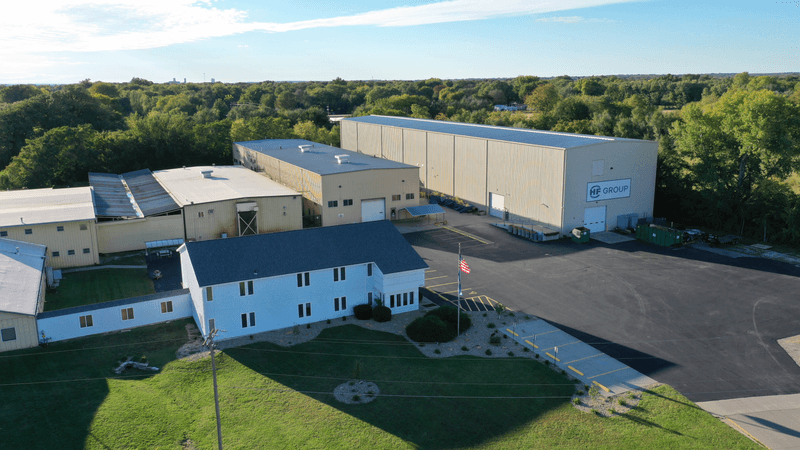 alt="Aerial view of the HF GROUP company building with adjacent production halls, surrounded by trees and green areas"