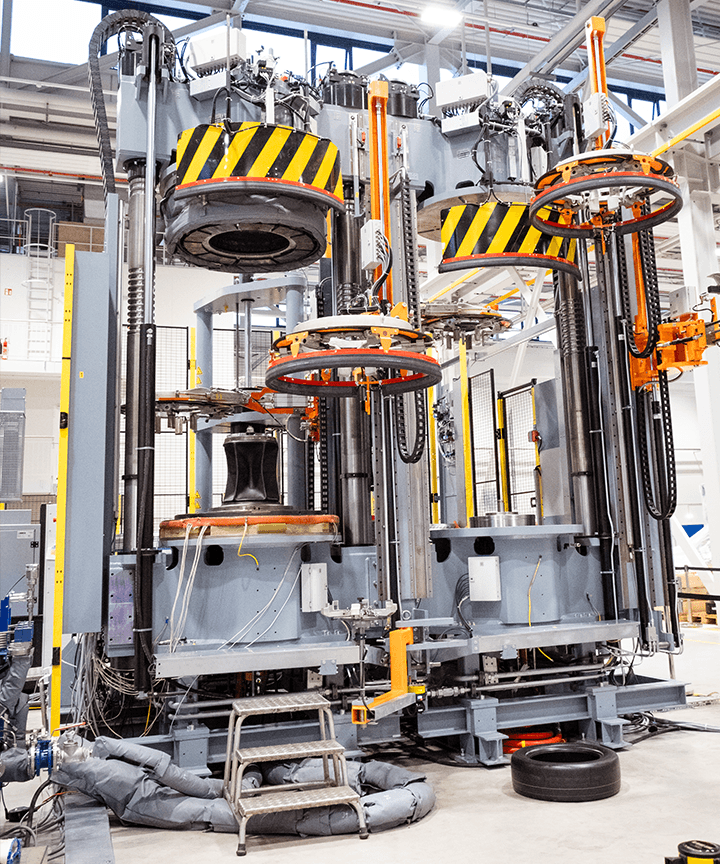 Tyre curing press with multiple press stations, lifting systems, and safety markings.