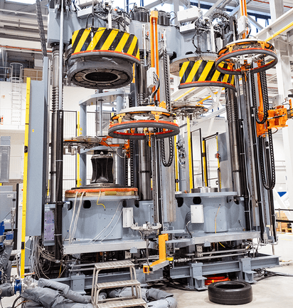 Tyre curing press with multiple press stations, lifting systems, and safety markings.