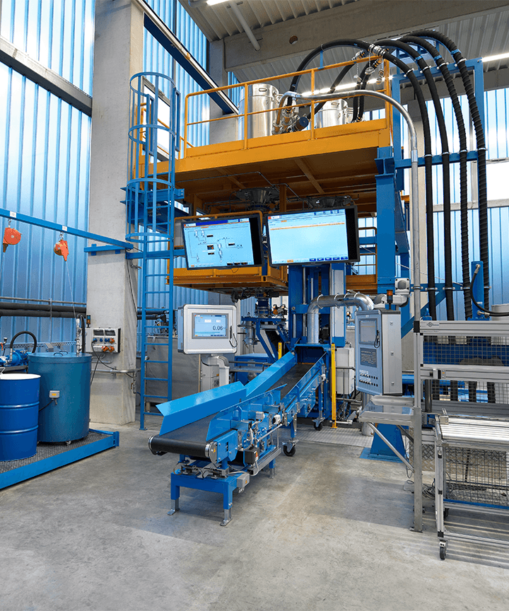 Industrial station with conveyor belt, control screens, barrels, and elevated equipment platform.